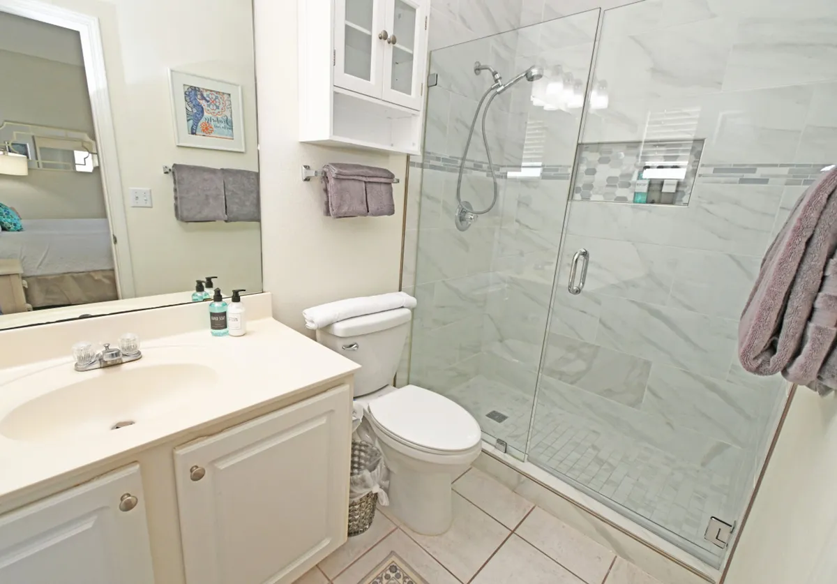 A modern bathroom interior with a glass-enclosed, tiled shower, a white vanity with a sink and mirror, and neatly folded towels on a wall-mounted cabinet. The space feels refreshing and spa-like, with clean finishes and a calm atmosphere.