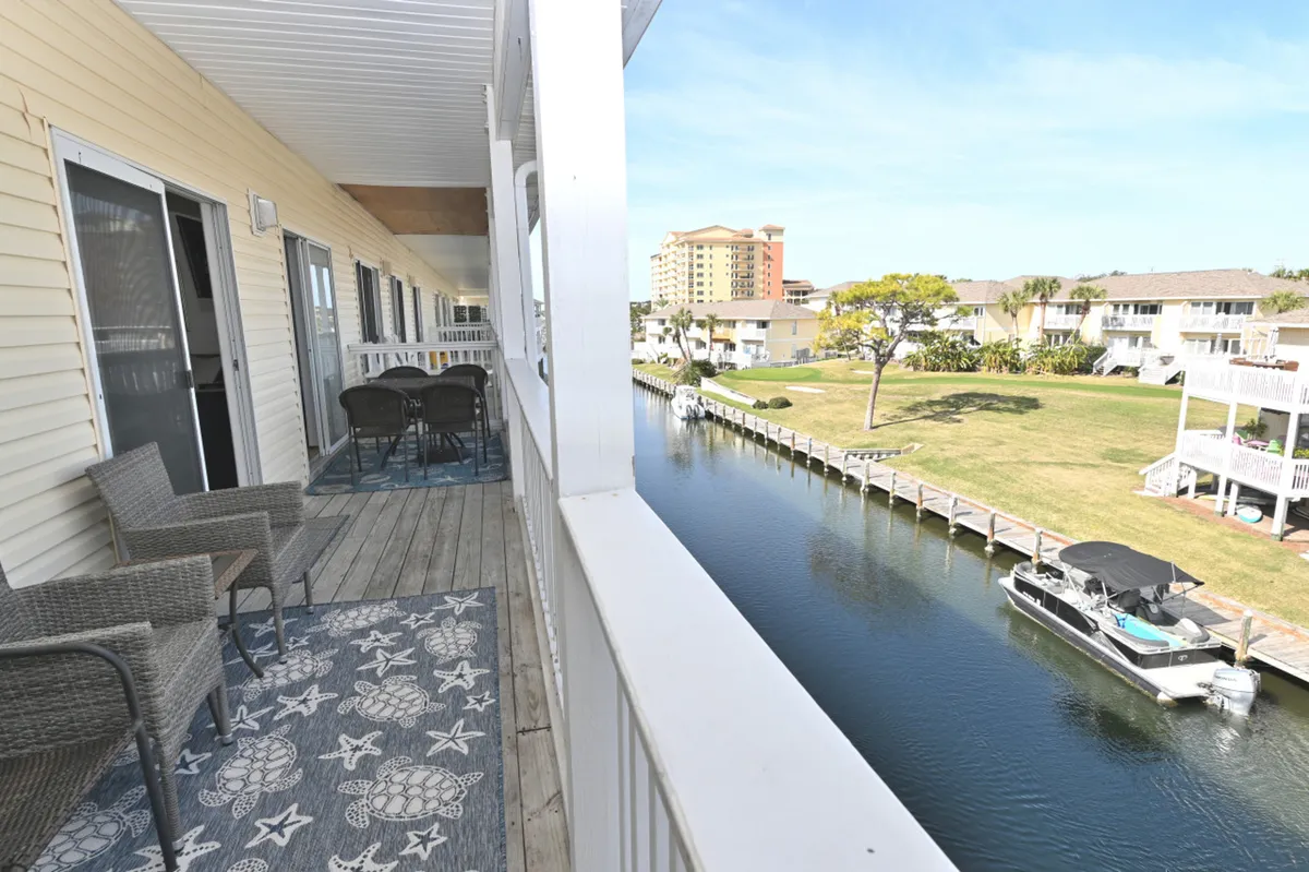 A peaceful canal scene with a docked boat, balcony seating area, and outdoor dining table. Neighboring waterfront properties are visible, and the setting is ideal for relaxing, enjoying canal views, and watching local wildlife.