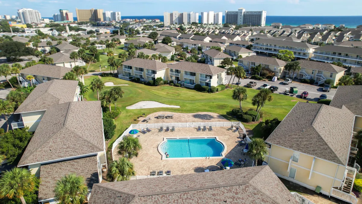 This inviting scene showcases a central swimming pool area surrounded by lounge chairs and balconies, with a nearby green golf course and a distant ocean and skyline view. The pool is a focal point for relaxation and play, embodying resort-style leisure.